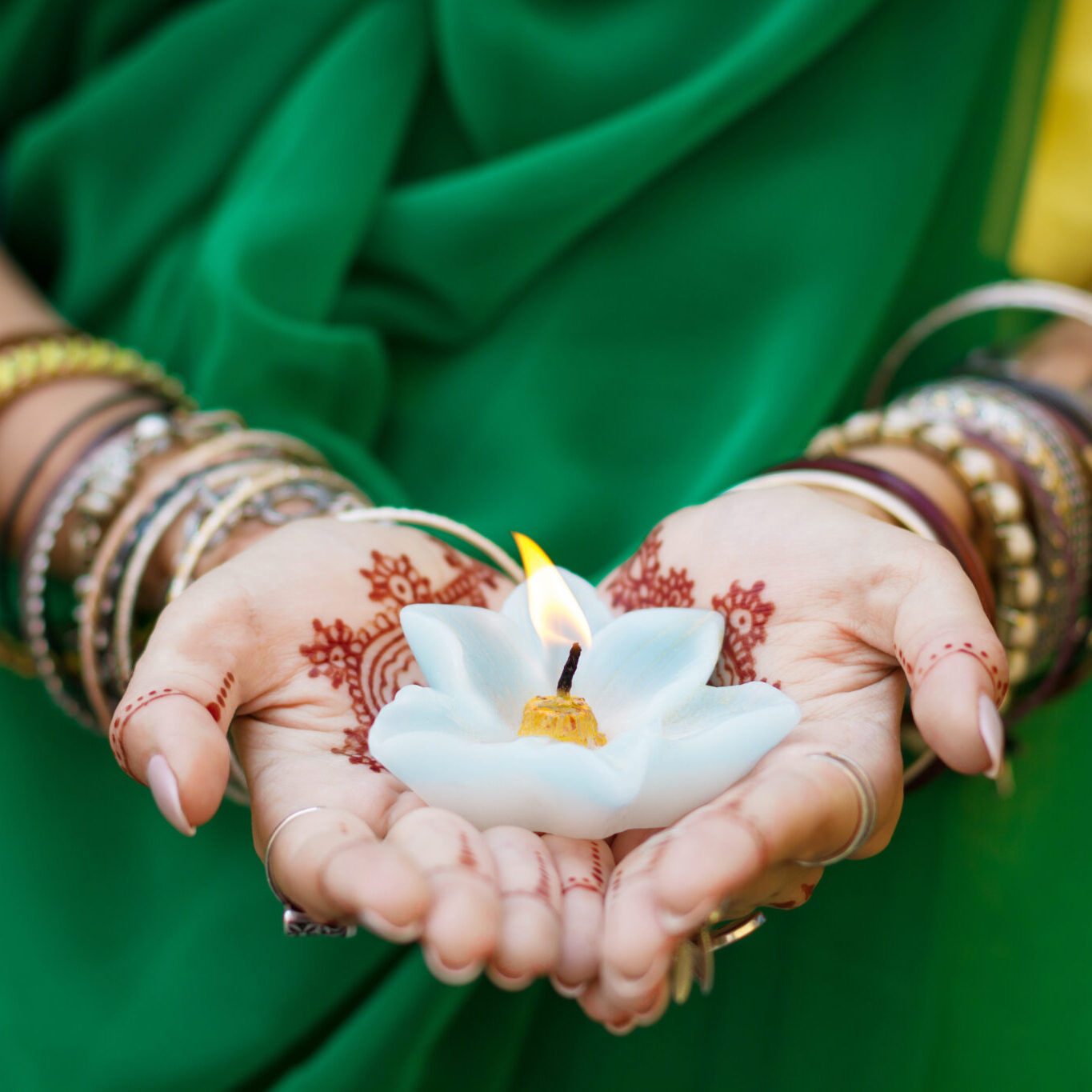 Beautiful woman in traditional Muslim Indian wedding green sari dress hands with henna tattoo mehndi pattern jewelry and bracelets hold burning lotus candle Summer culture festival celebration concept